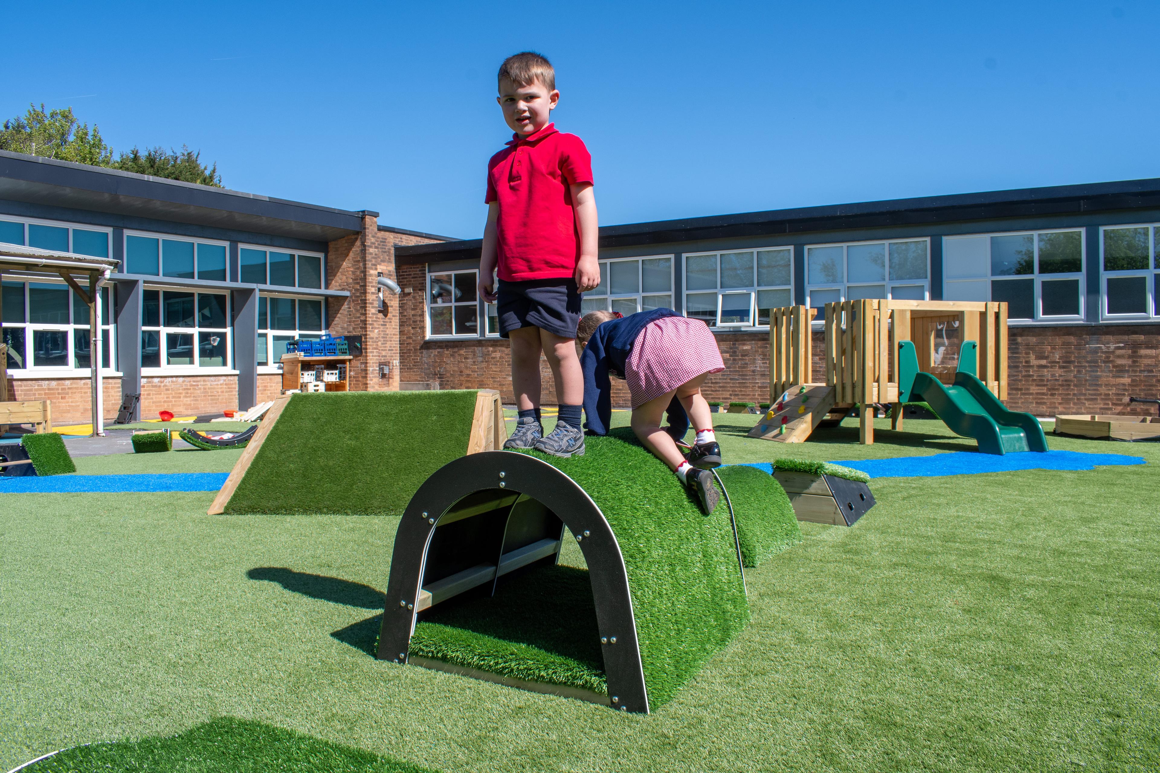 A boy is stood on top of the tunnel block, looking at the camera. A girl is crawling on top of it too, behind the boy.