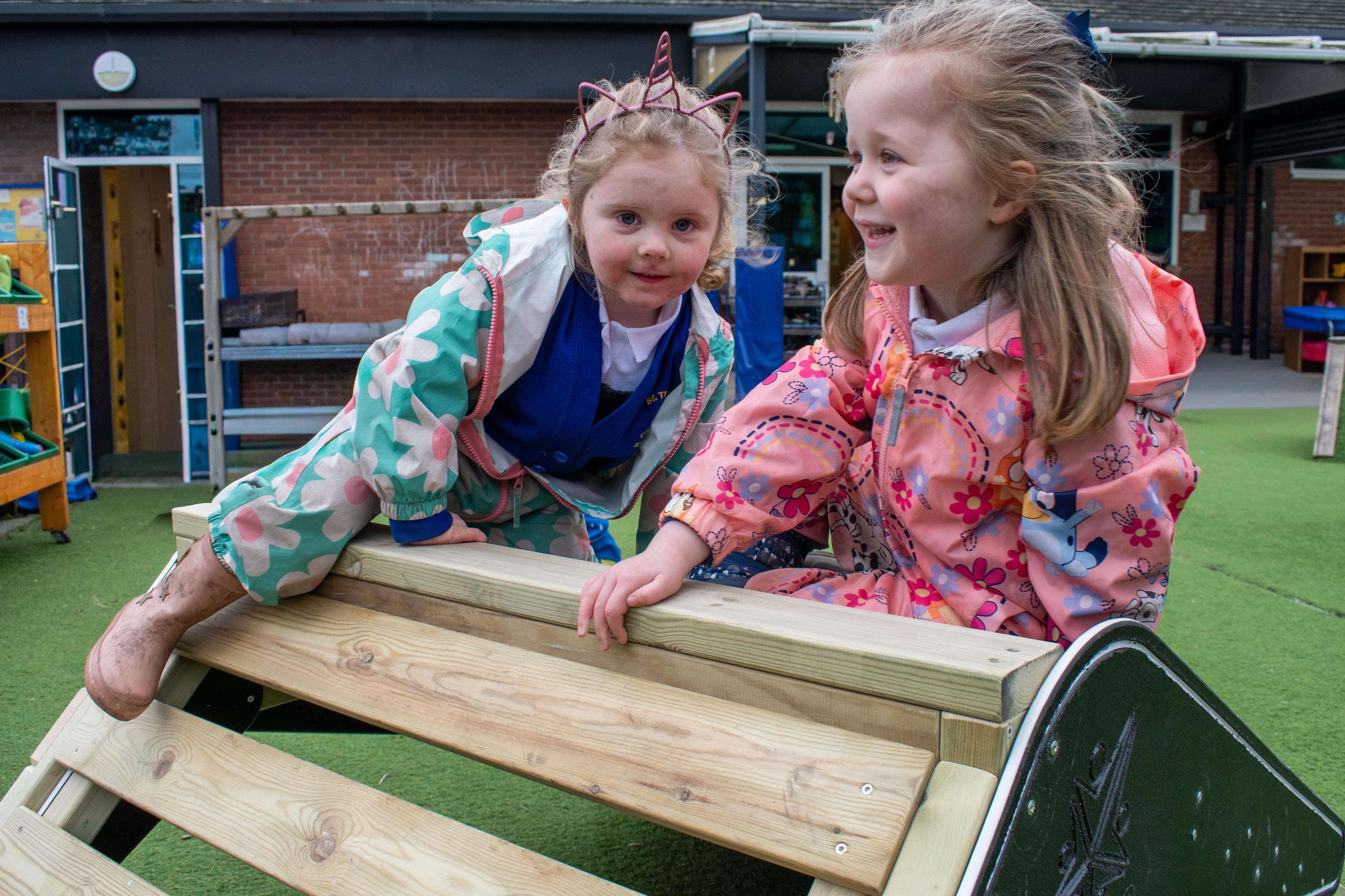 Two children are at the top of the A-frame, climbing over to the wooden ladder section.