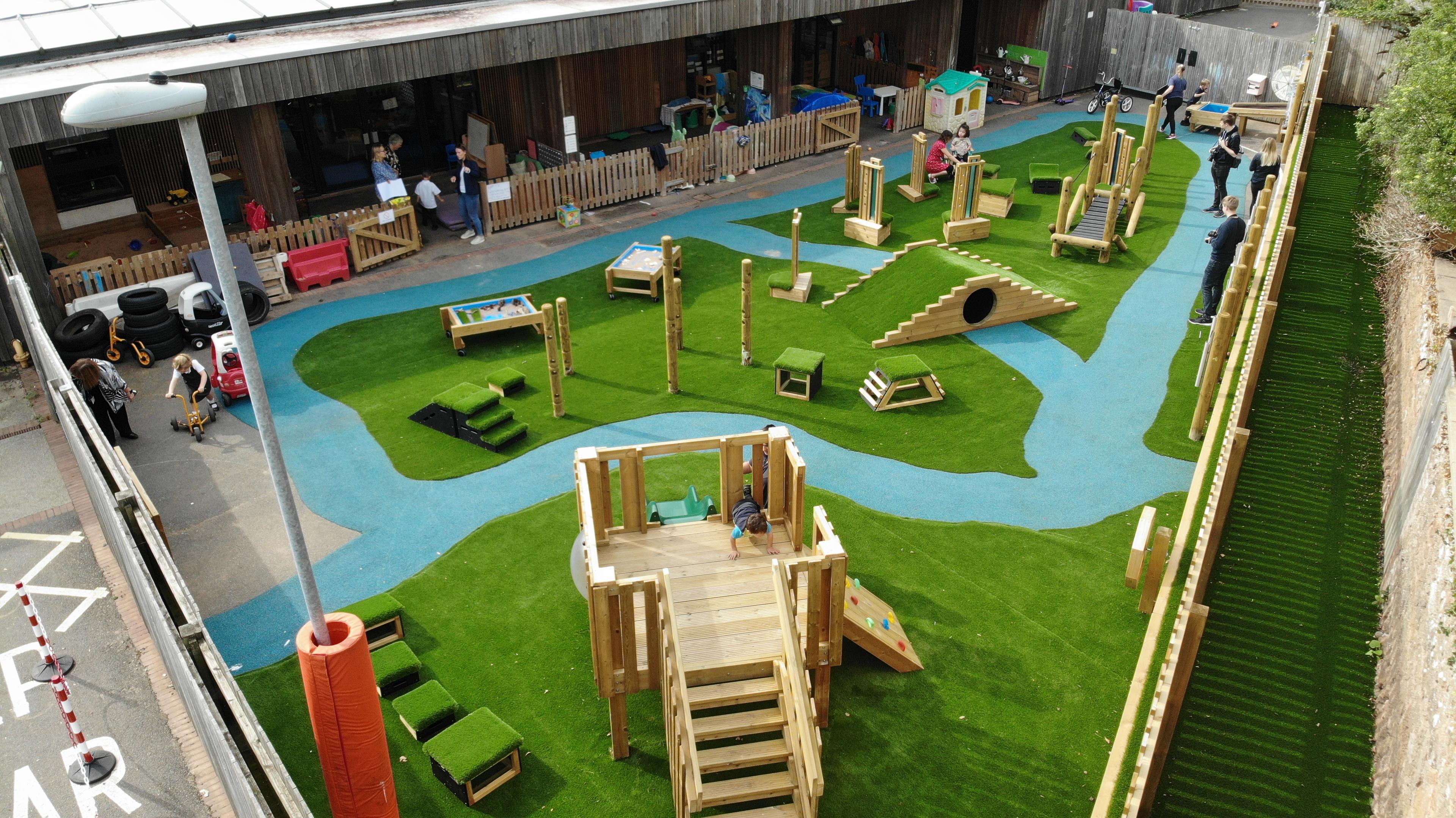 A playground scheme with a play towel, crawl-through tunnel and more. Surfaced in artificial grass and blue wet pour.