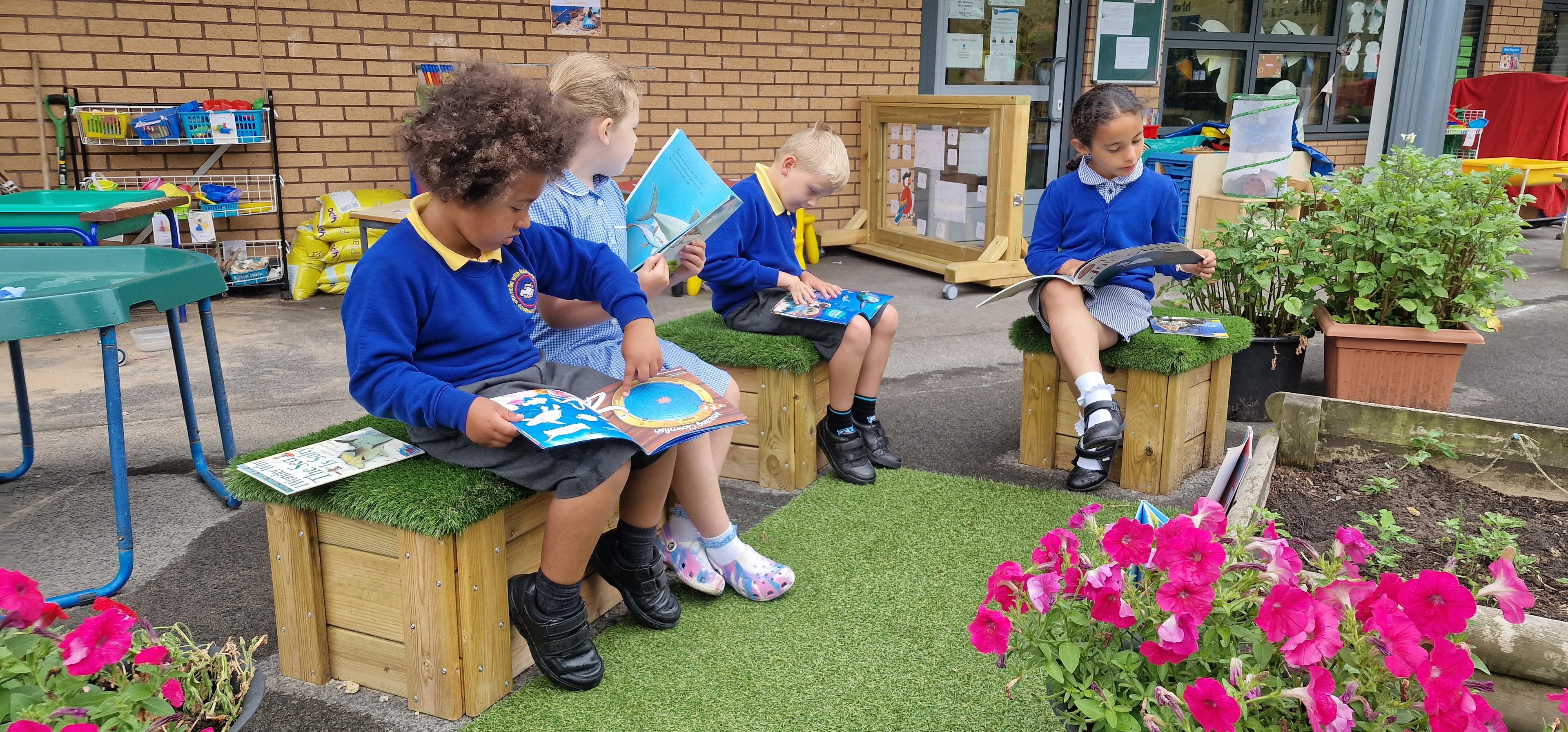 A group of children sat on artificial grass-topped seats and reading.