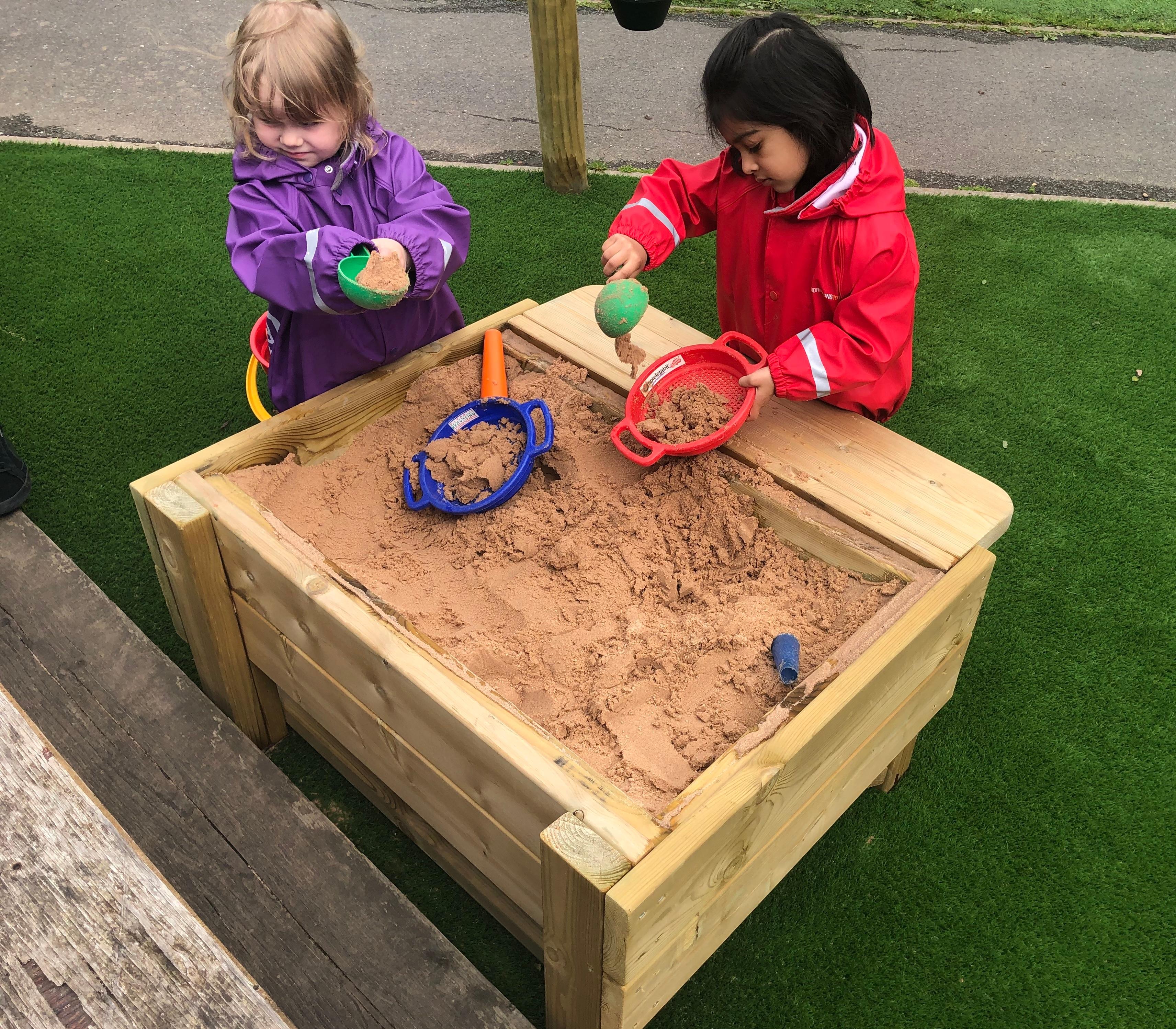 A photo of two nursery children playing in a sand table.