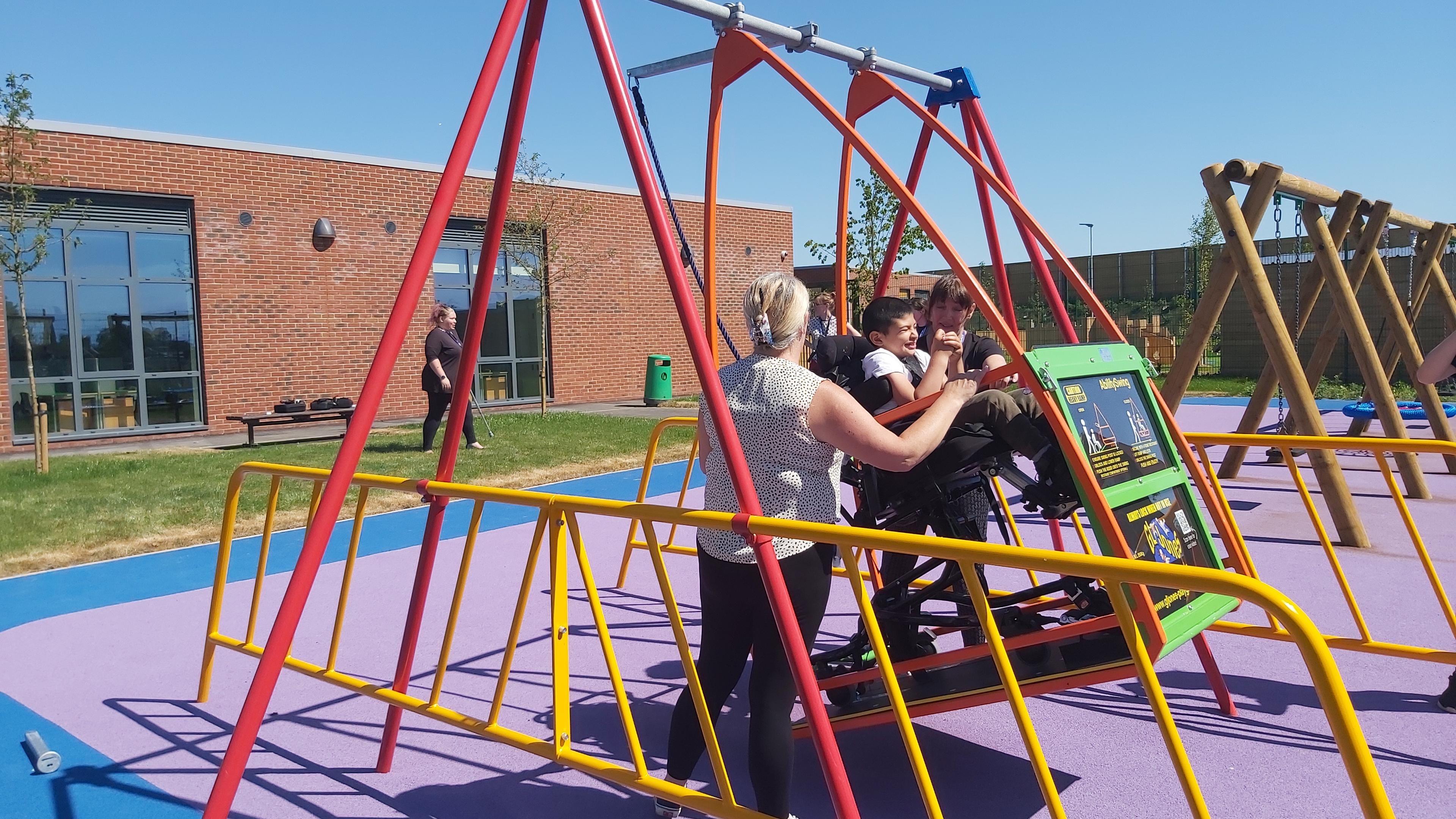 A group of school children in purple and teal sweaters climb and balance on the timber beams and ropes of a Pentagon Play Tryfan Climber over green safety surfacing.