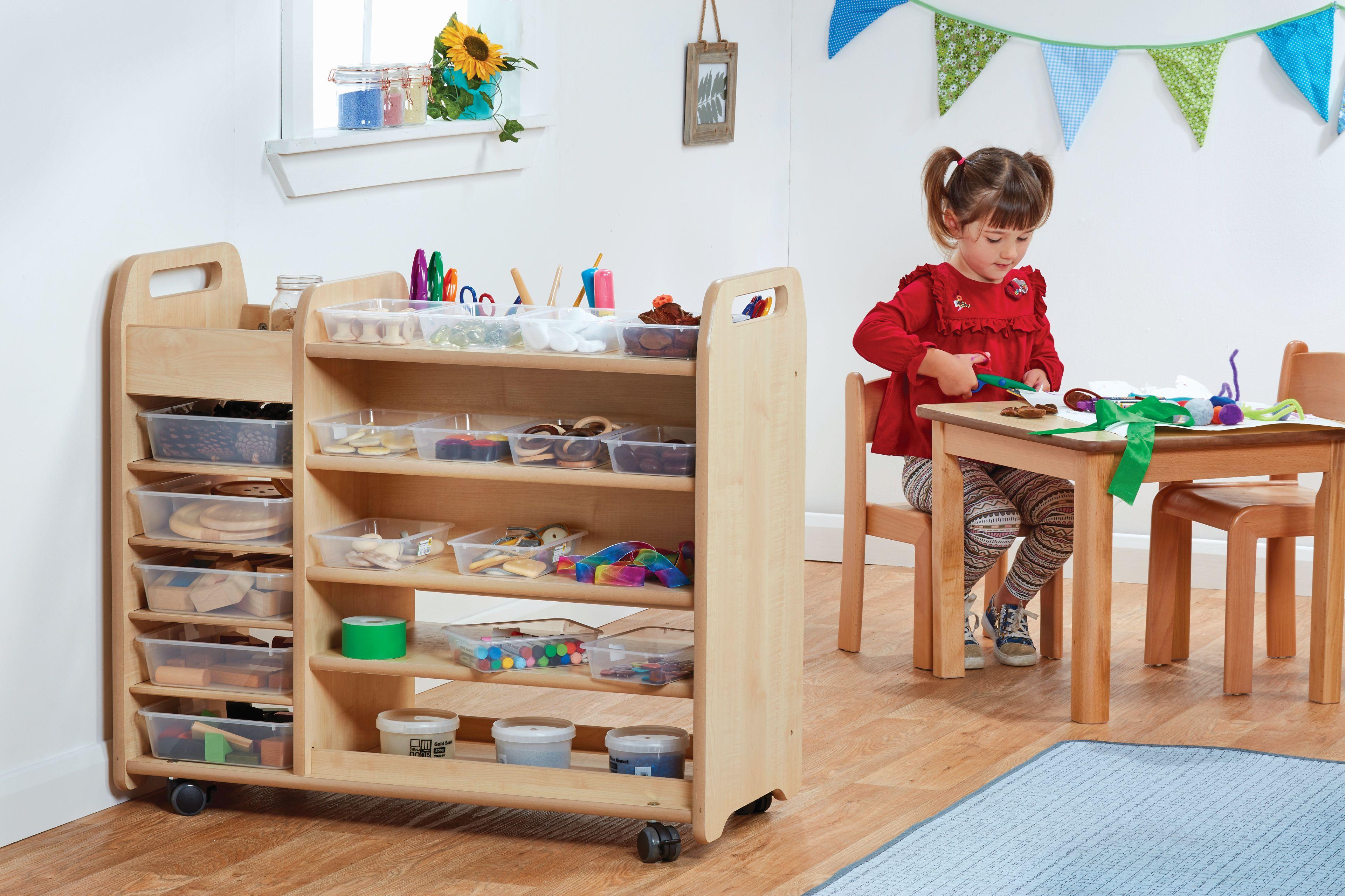 A studio photo with some movable storage shelves and a set of table and chairs in the background. A child is sitting at the table doing crafts.