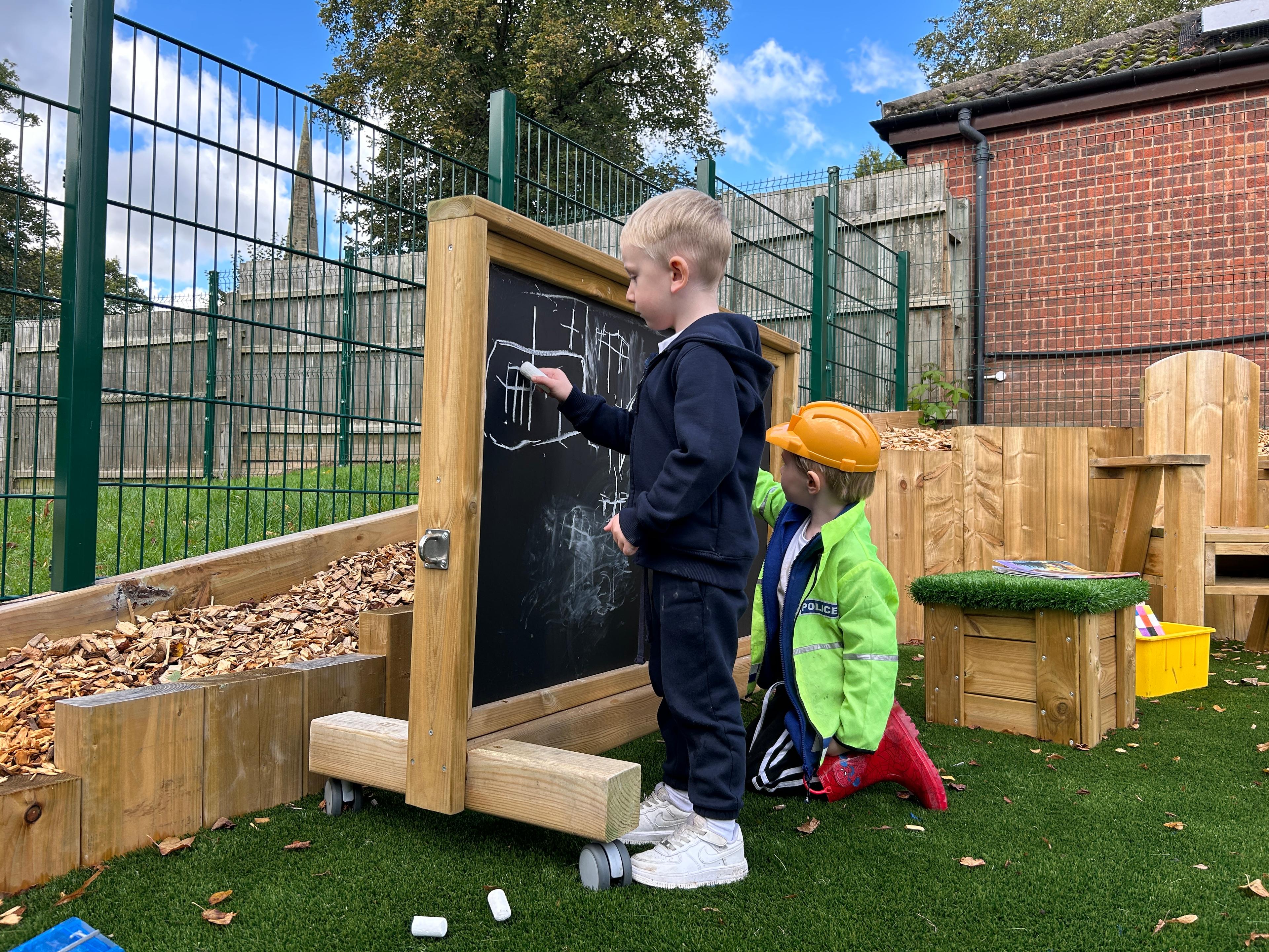 A photo of two children writing on a movable chalkboard panel.