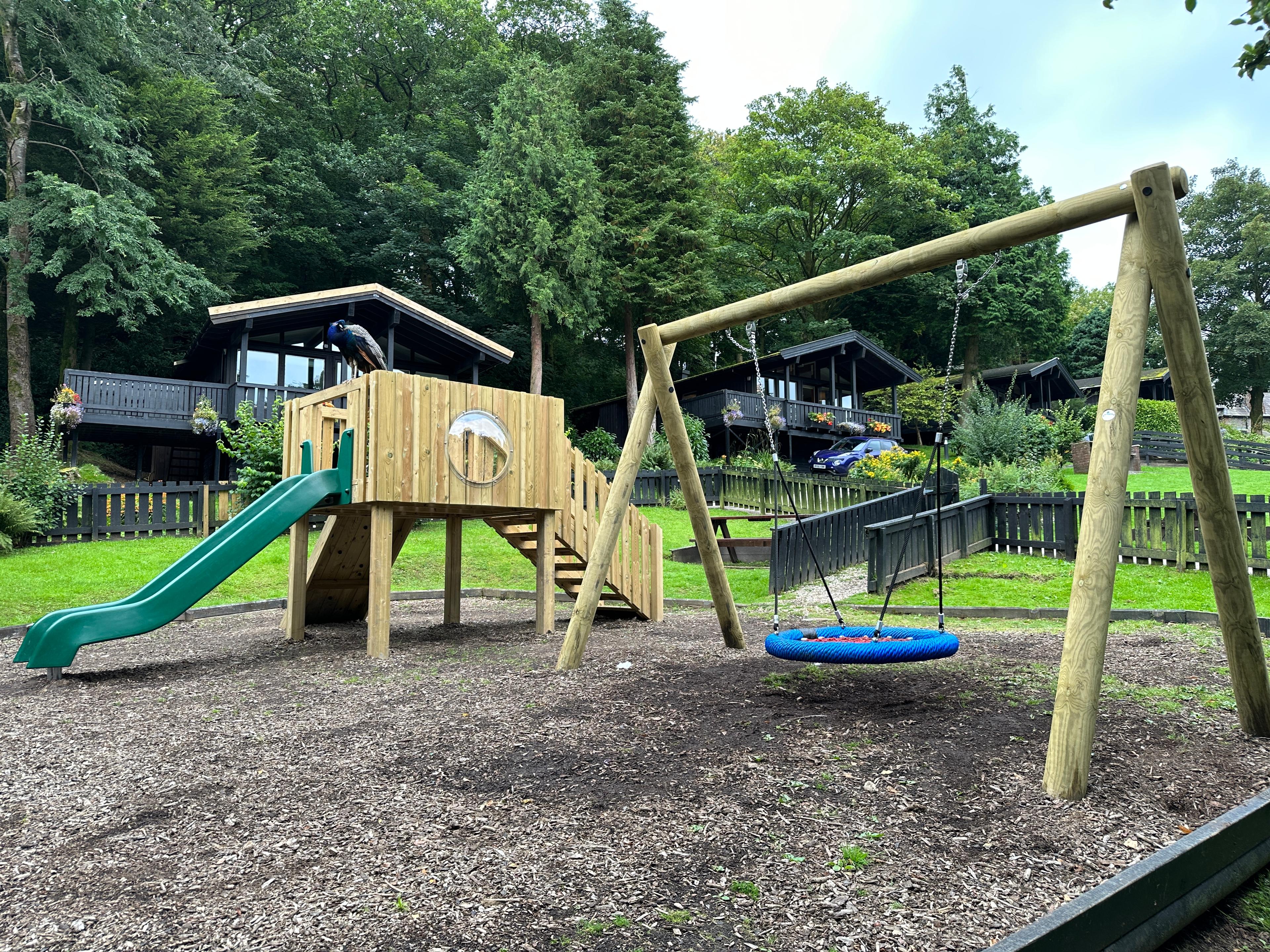 A photo of a play tower and a group timber swing in the middle of a holiday park with cabins,