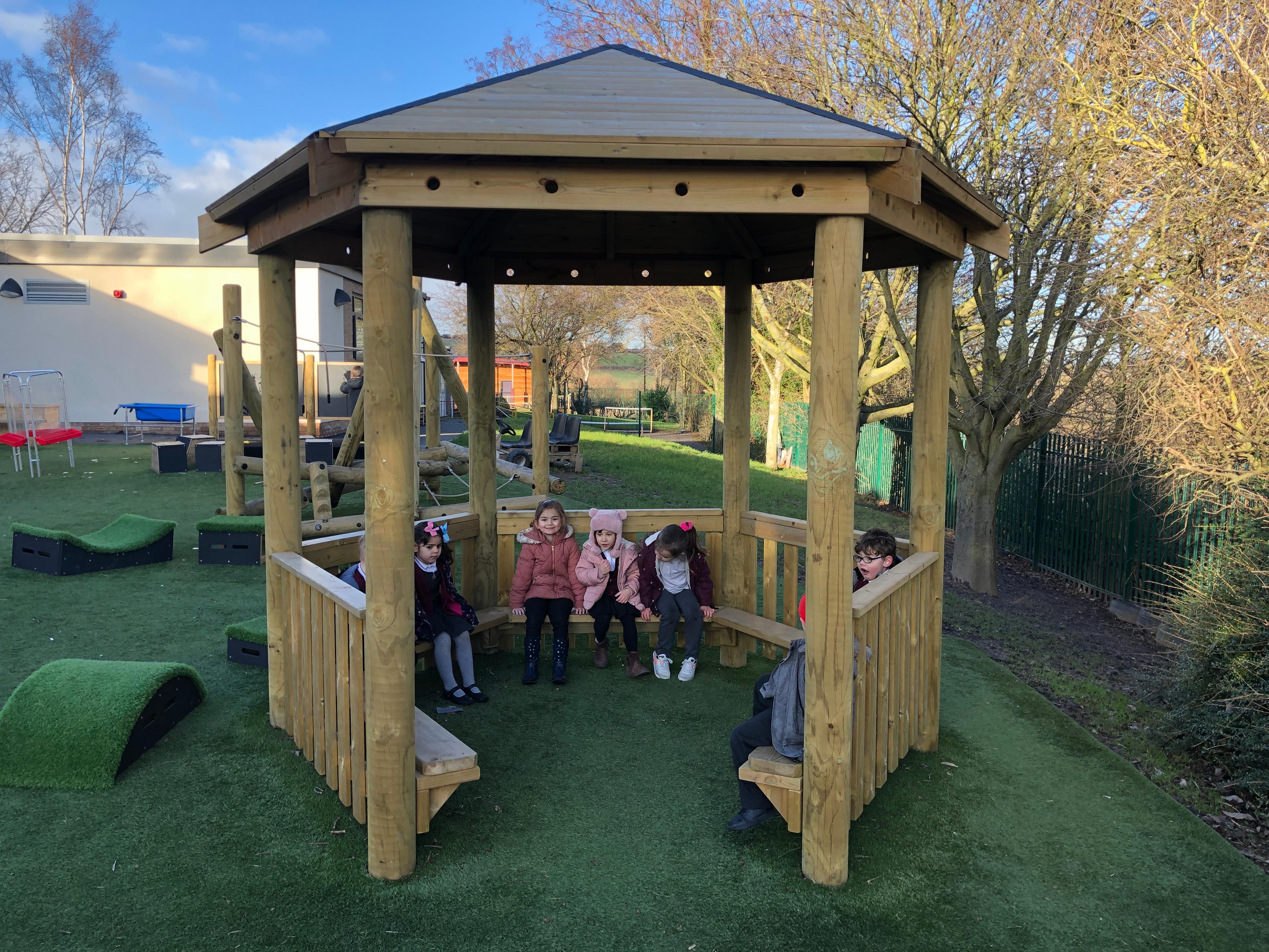 A photo of a 3.5M gazebo with young nursery children sat inside smiling.