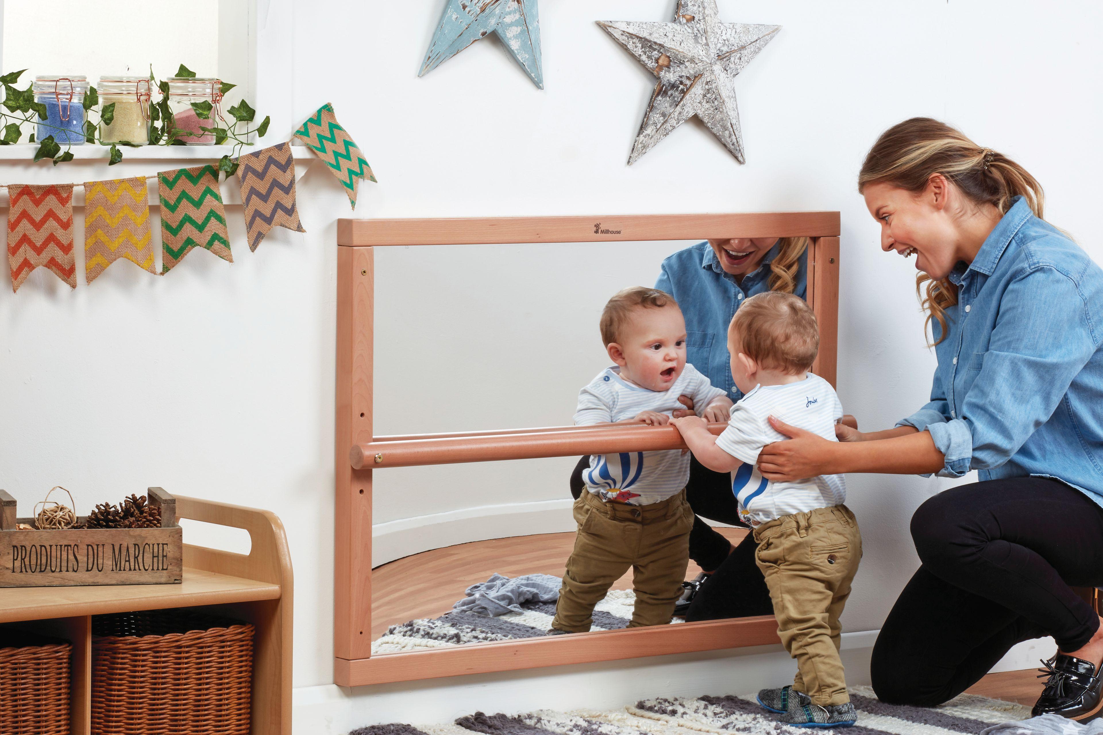 A nursery teacher holding up a baby in a mirror panel.