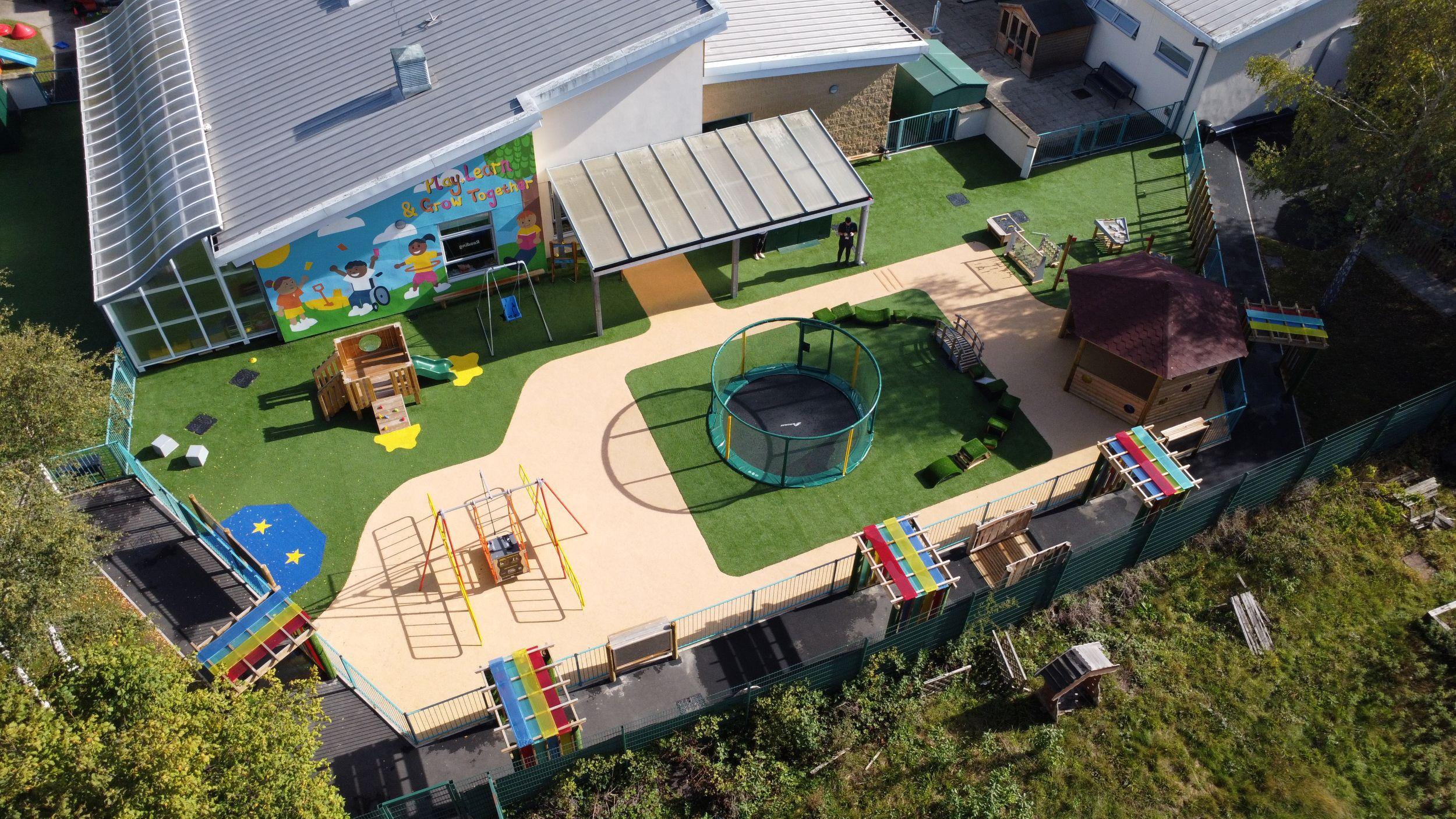 SEN playground featuring an in-ground trampoline and small play tower on artificial grass. A path is covered by multiple Sensory Arbours, with a large Hexagonal Gazebo.